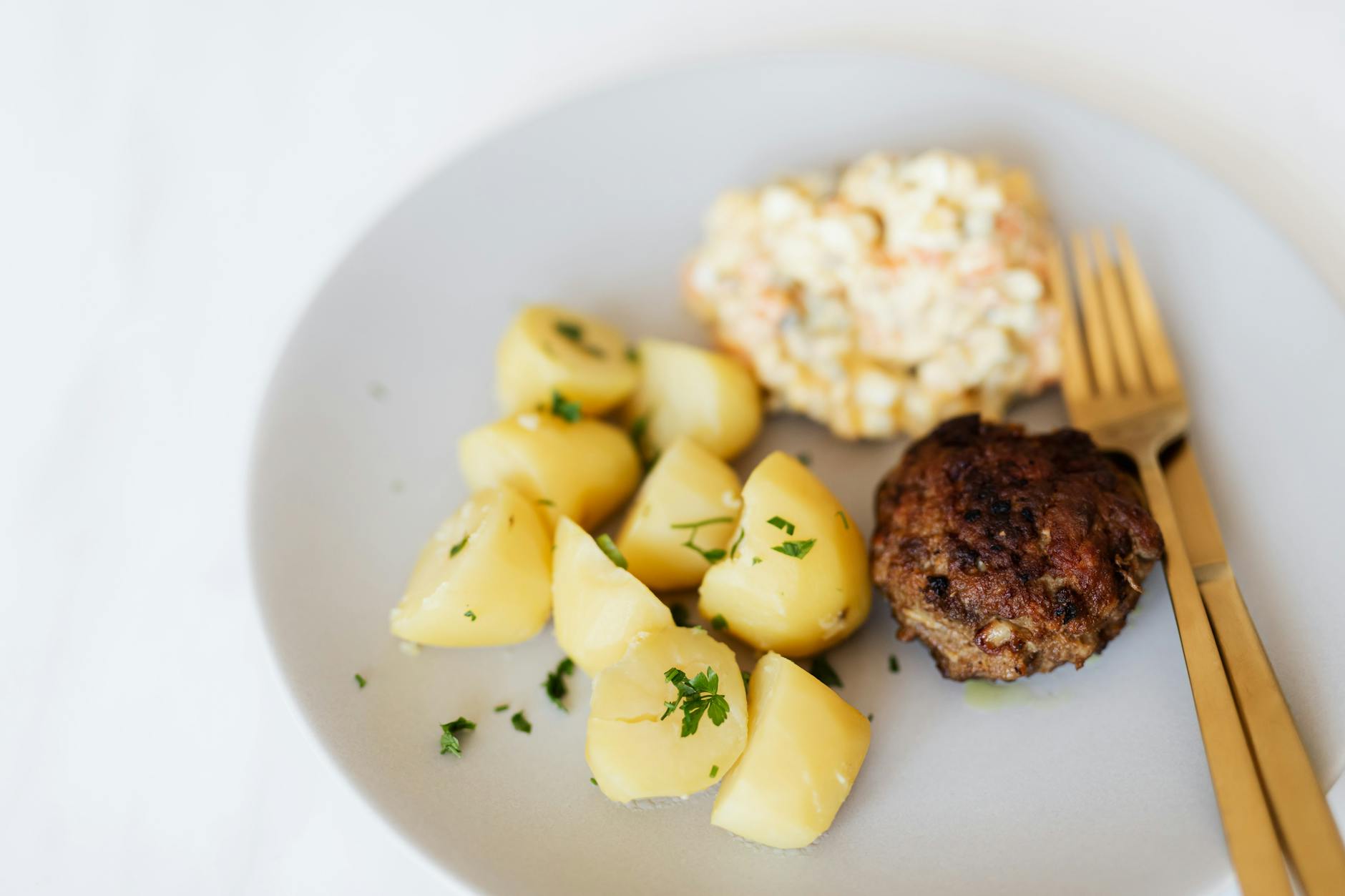 Domowy obiad: kotlet mielony, ziemniaki i sałatka na białym talerzu
