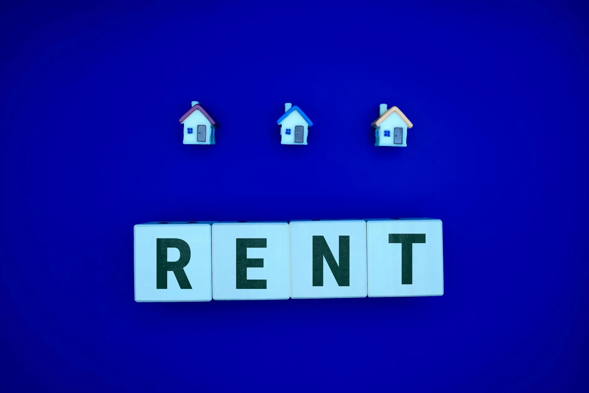 Miniaturowe domki nad napisem RENT na niebieskim tle, inwestycja na wynajem