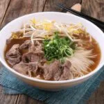 Miska domowej zupy pho z wołowiną, makaronem ryżowym i ziołami